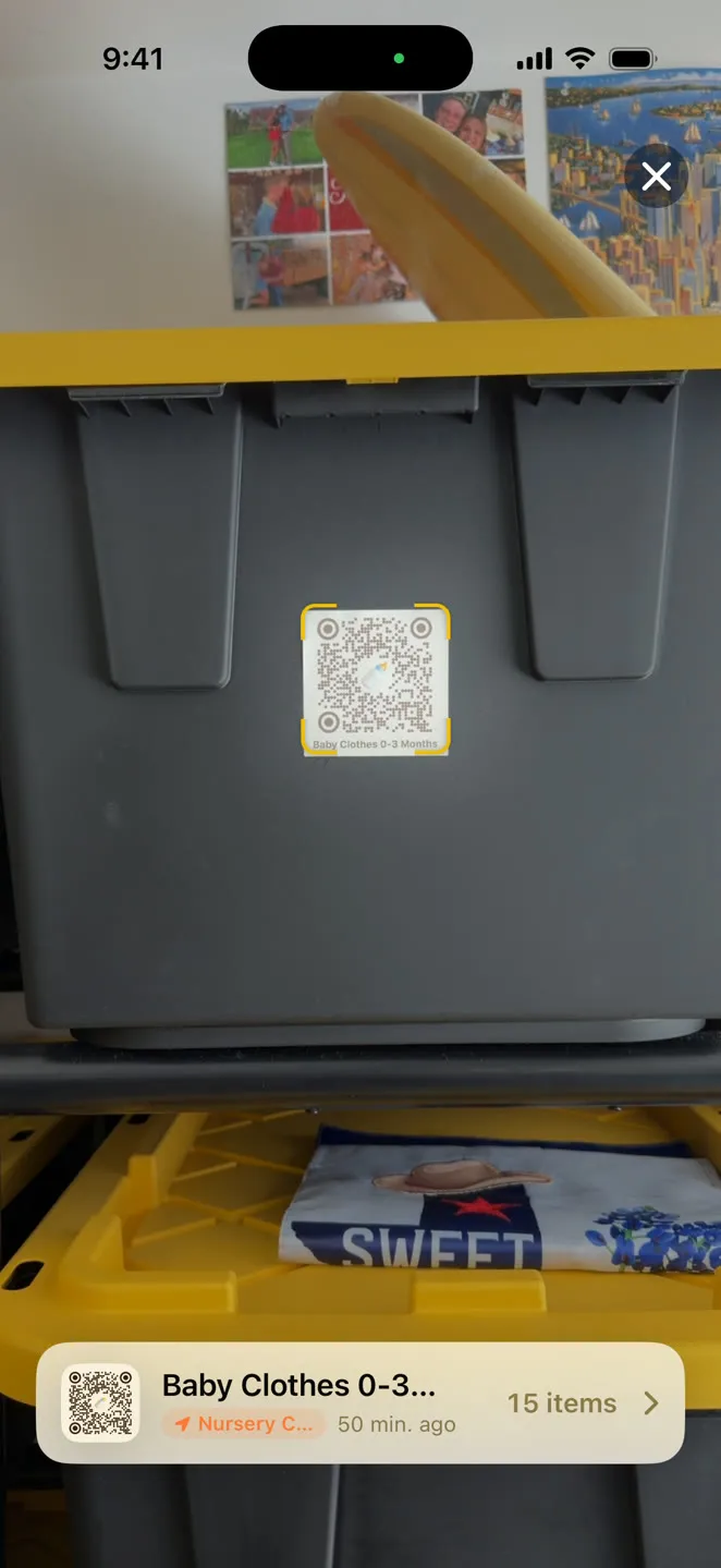 StowQR on iPhone scanning a QR label on a gray storage tote and showing the Baby Clothes tote it belongs to